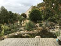 Der Blick von einem Holzdeck auf den Gartenteich, in den das Wasser des Bachlaufes am Ende hineinflie&szlig;t (in Paris).